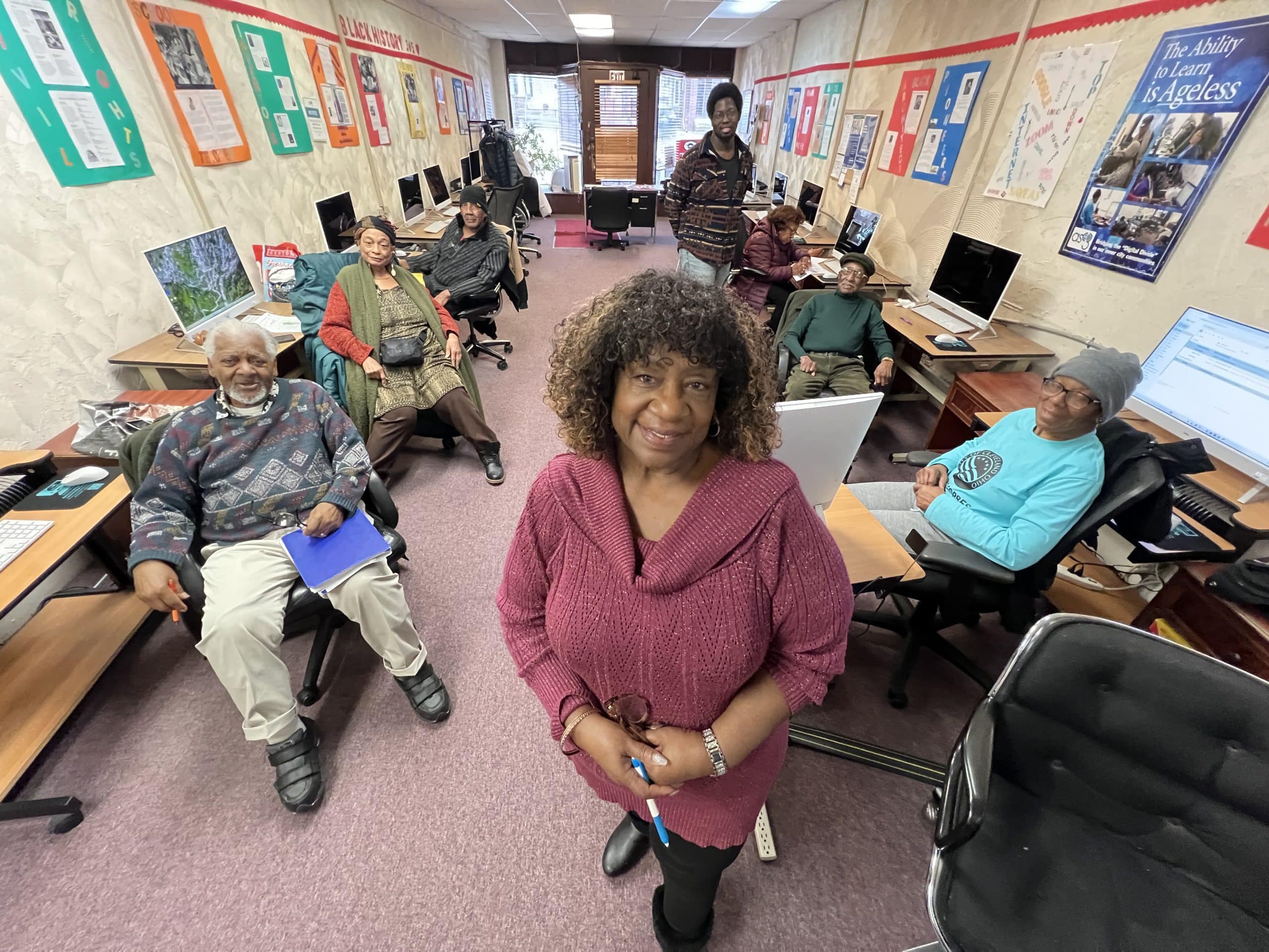 Older adults learning at computers in a warm community center with a helper nearby